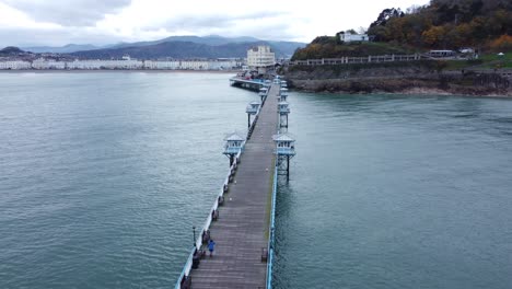 Llandudno-Pier-Icónico-Histórico-Victoriano-De-Madera-Junto-Al-Mar-Punto-De-Referencia-Vista-Aérea-Volando-Sobre-El-Paseo-Marítimo