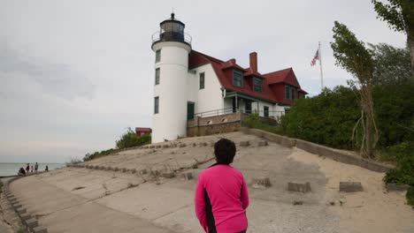 Mujer-Caminando-Cerca-Del-Faro-De-Punto-Histórico-Betsie-En-Frankfort,-Michigan-A-Lo-Largo-Del-Lago-Michigan-Con-Video-De-Cardán-Desde-Atrás-En-Cámara-Lenta