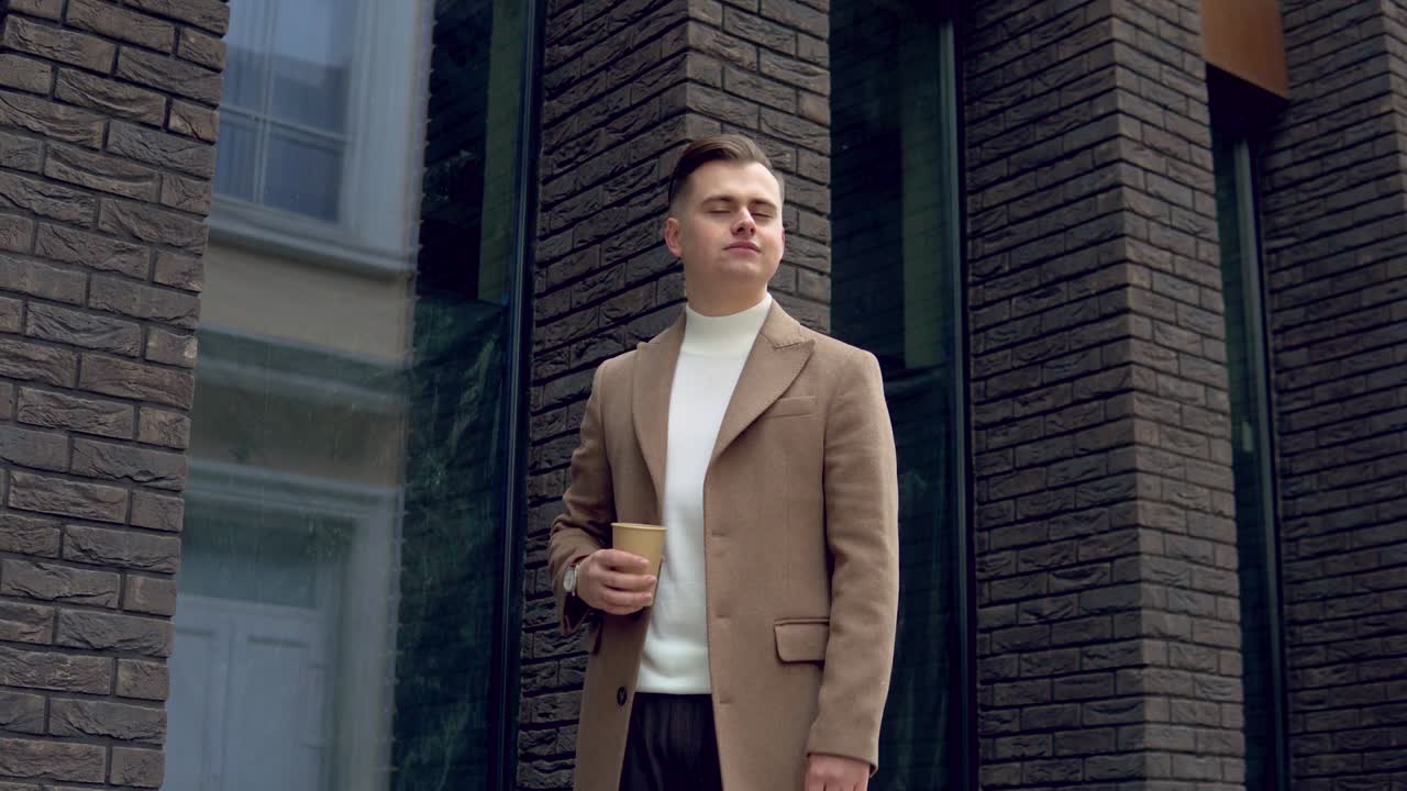 Handsome businessman in brown coat with coffee near the office