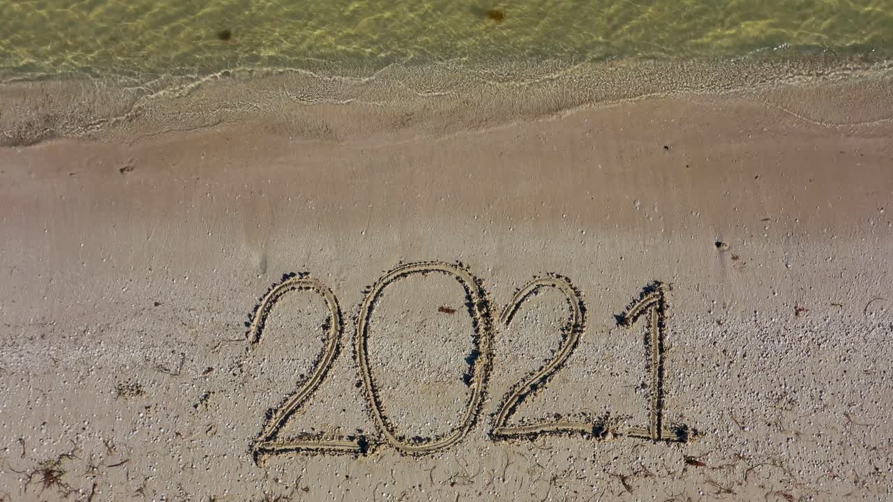 veinte veintiuno escrito en la arena llena el encuadre y se hace más pequeño a medida que la cámara se aleja manteniendo la fecha en la parte inferior del encuadre