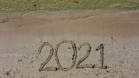 twenty twenty one written in the sand fills the frame and gets smaller as the camera moves away keeping the date at the bottom of the frame