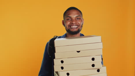 male pizzeria courier carrying huge pile of pizza boxes in studio