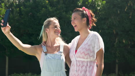 two female friends enjoying sunny day by pool, looking at smartphone together