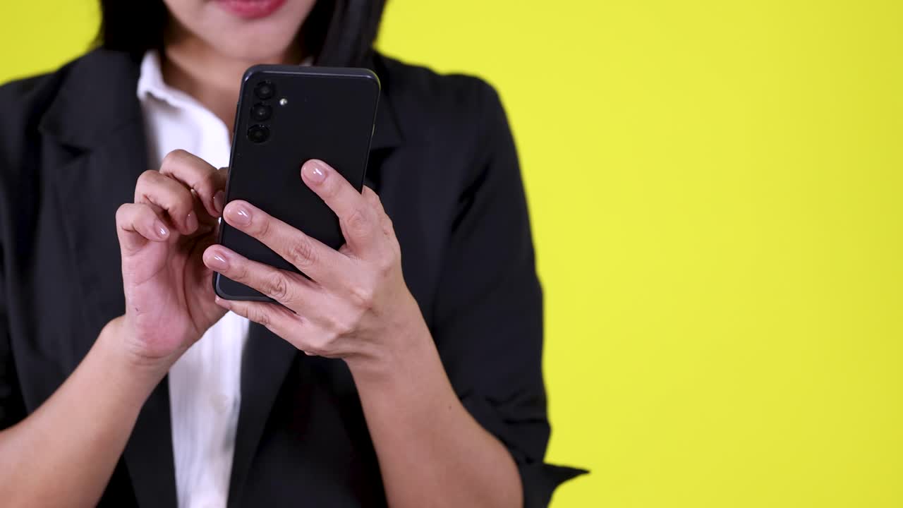 Close-up of professional woman typing on smartphone, static camera, bright studio lighting, yellow backdrop