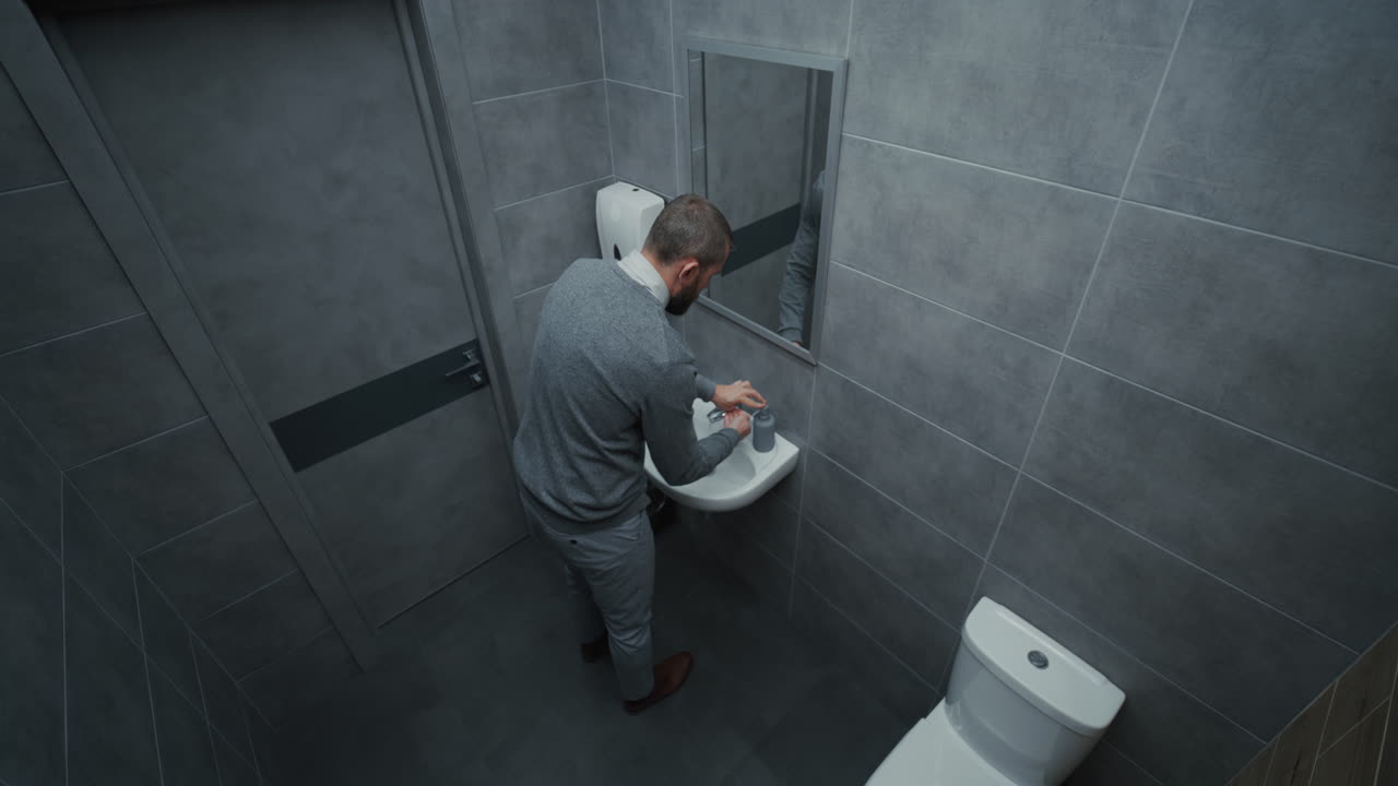 Businessman Looking in the Mirror Washing His Hands with Soap in Restroom of Modern Office