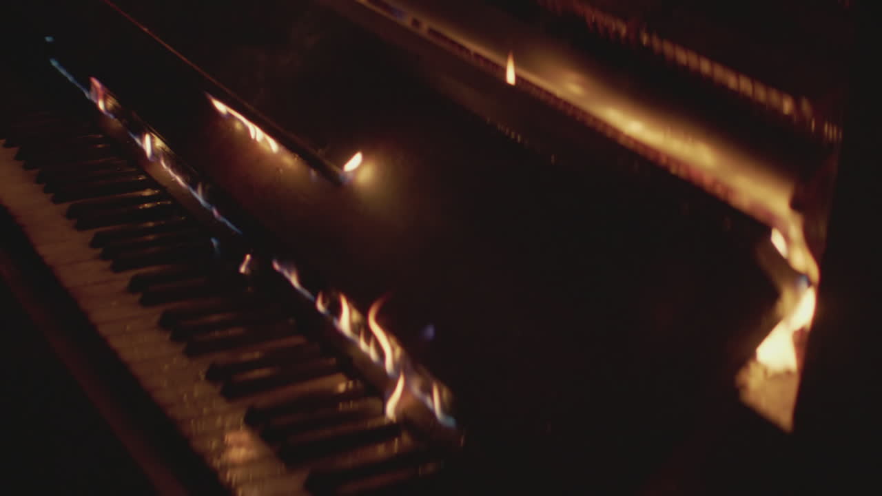 A fire burns up a piano in the dark