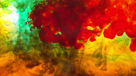 green red and orange paint or dye dropped into water against white background to create swirling colourful smoke background