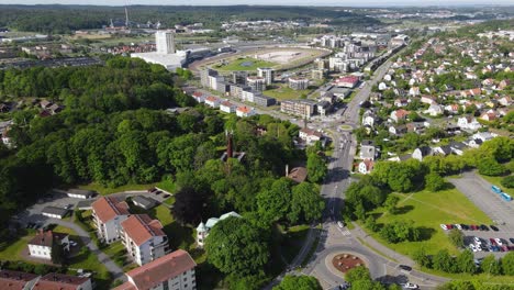 drone flying over the lush trees and apartment buildings in frolunda, gothenburg, sweden with vehicles travelling on the road on a sunny day - aerial