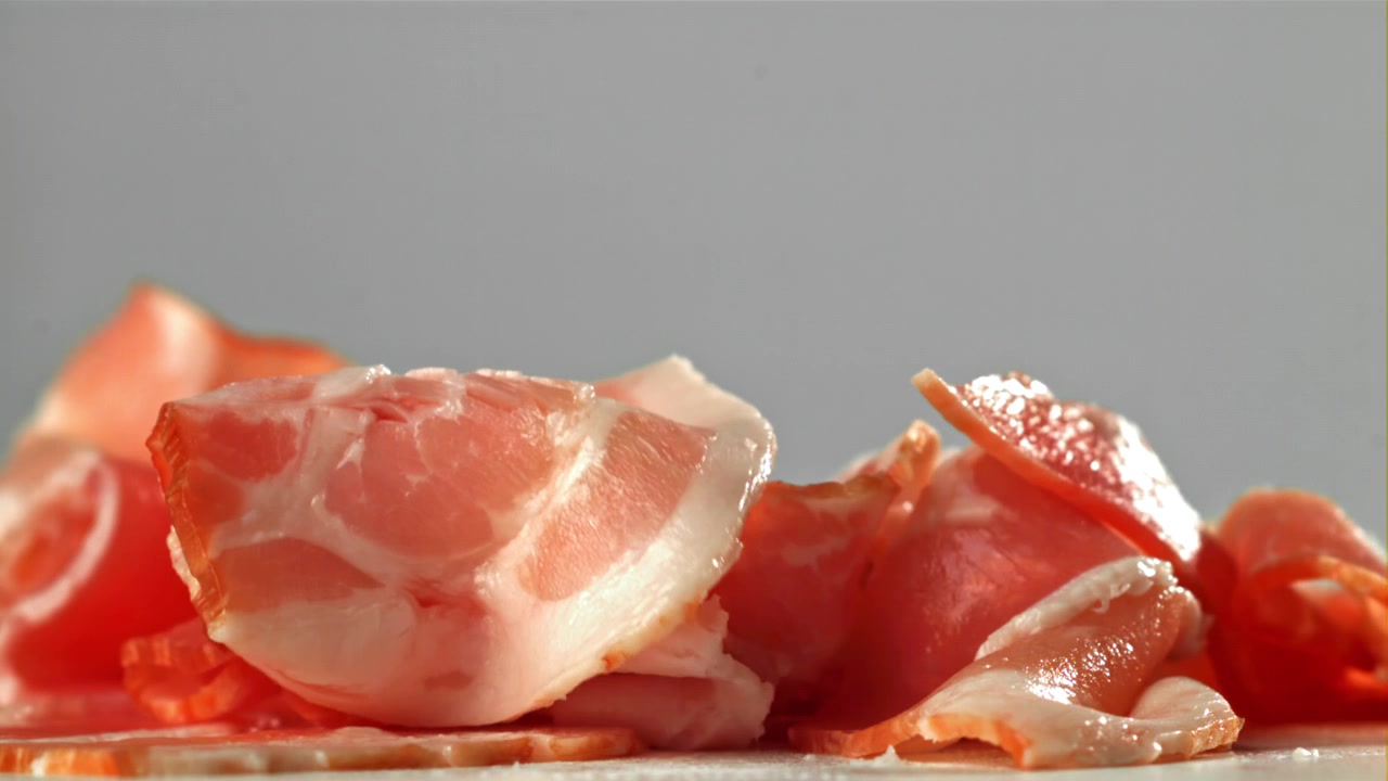Fette di pancetta cruda che cadono al rallentatore