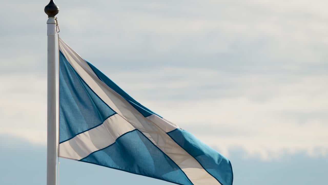 Scottish flag flutters on flagpole against cloudy sky, daylight, static camera, gentle breeze