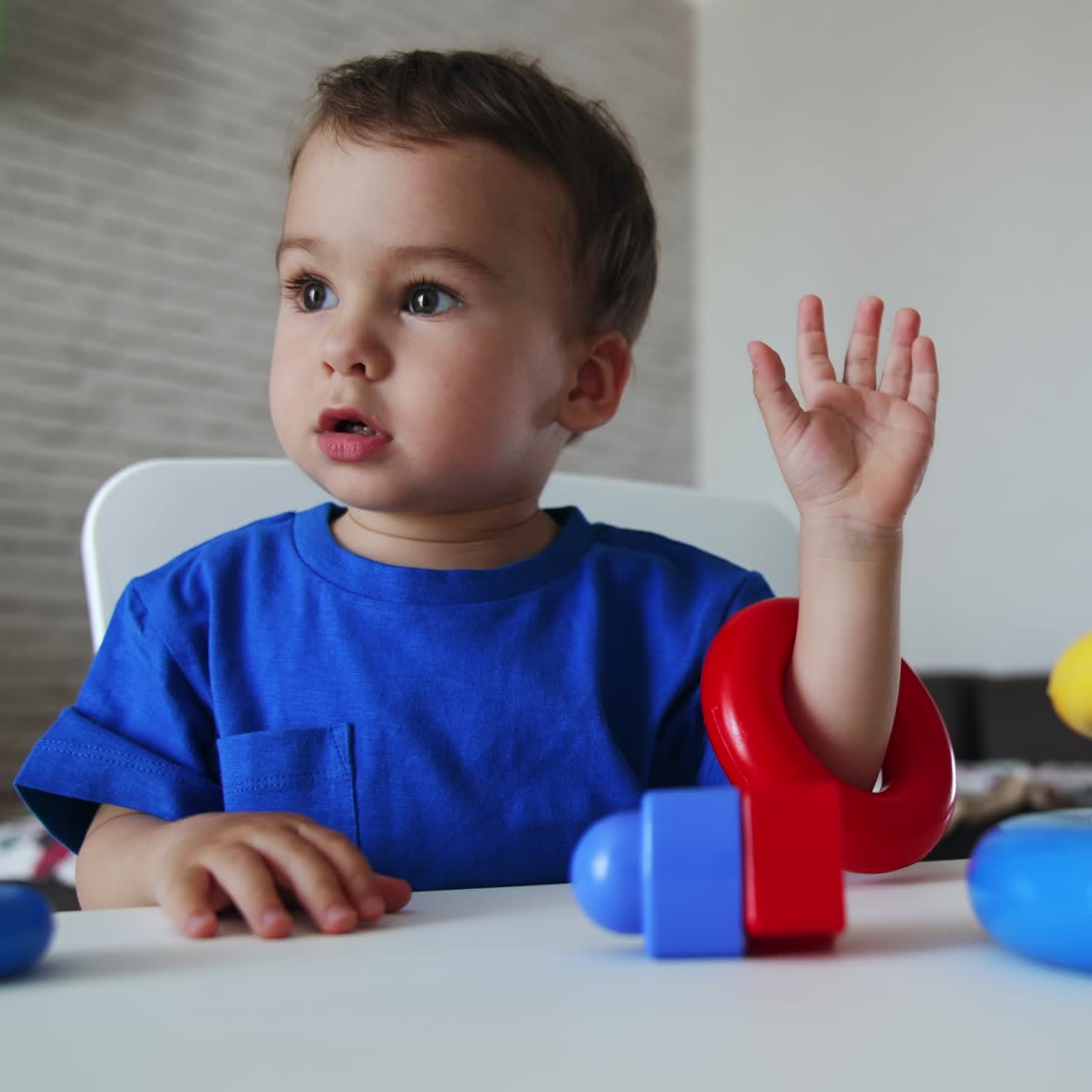 Lovely child assembling the colorful pyramid. Dark-haired kid puts on the rings from a toy on little hands