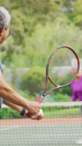 video de un hombre mayor biracial feliz sosteniendo una raqueta y comenzando el partido en la cancha de tenis