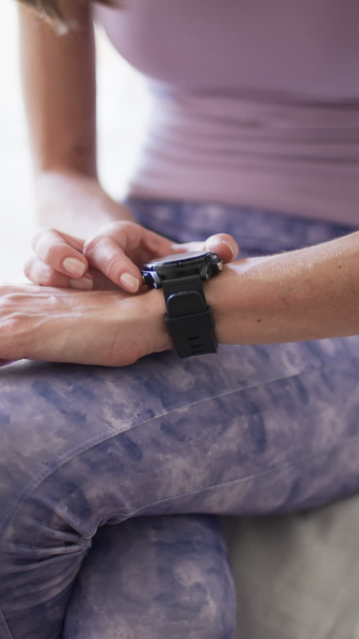 Vertical video: Caucasian woman checking smartwatch, at home