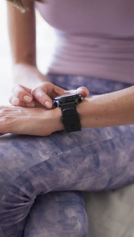 vertical video: caucasian woman checking smartwatch, at home