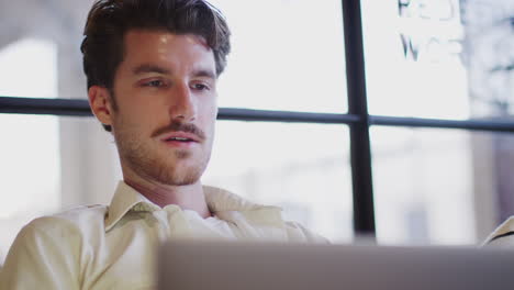 joven blanco trabajando en una computadora portátil, ángulo bajo, cabeza y hombros