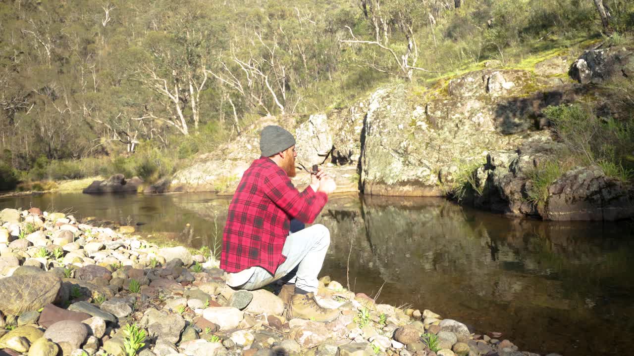 un bosquimano fuma una pipa junto a un río en el alto país victoriano