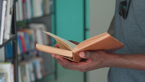 close up of adult holding open vintage book with worn pages while browsing in library, standing near shelves filled with books, creating atmosphere of focus, curiosity, and quiet learning