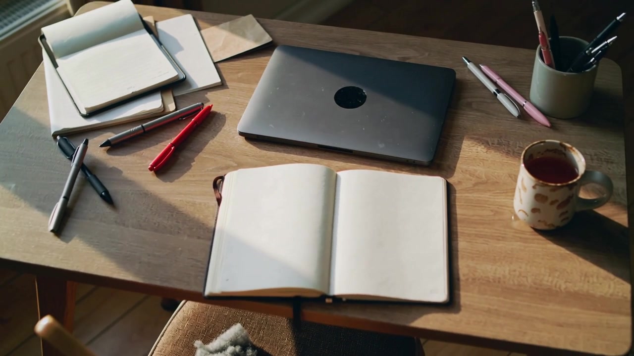 Sunlight shifting, camera panning, capturing open blank journal on study table with laptop, mug