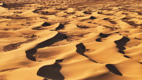 Telephoto-drone-shot-tilting-over-a-sunlit-sand-dunes-of-a-remote-desert