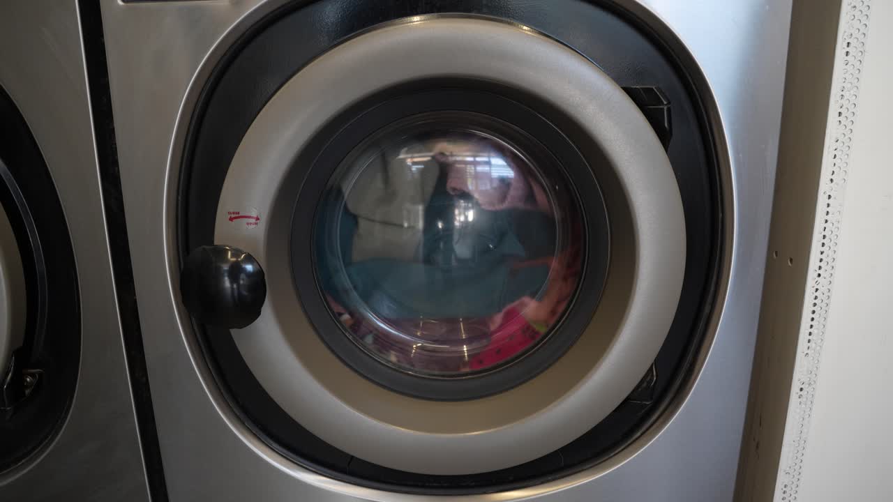 Front loading silver washing machine spins and sorts clothes in laundromat