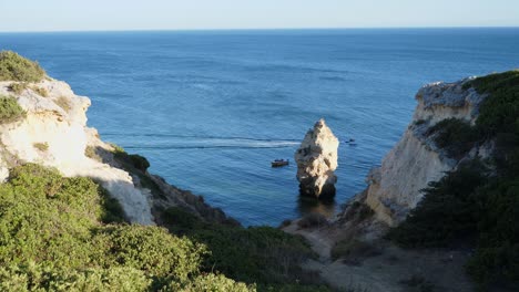 Establishing-shot,-Scenic-view-of-the-trail-going-to-the-rock-tunnel-beach-in-Algarve,-Portugal,-a-boat-passing-by-on-the-sea-in-the-background