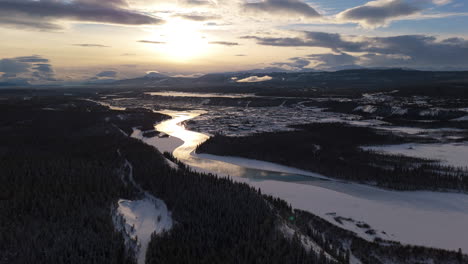 a smooth aerial shot capturing the stunning sunset over the rugged landscape surrounding downtown whitehorse and the yukon river, showcasing the natural beauty of the yukon.