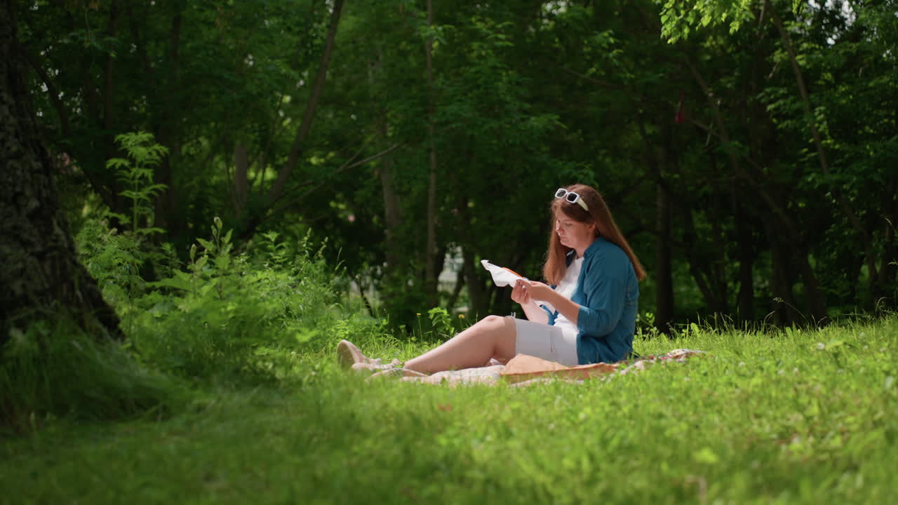 Fashion designer embroidering white fabric in serene park, seated under trees with gently swaying leaves, focused on delicate stitching work, surrounded by soft sunlight and lush greenery