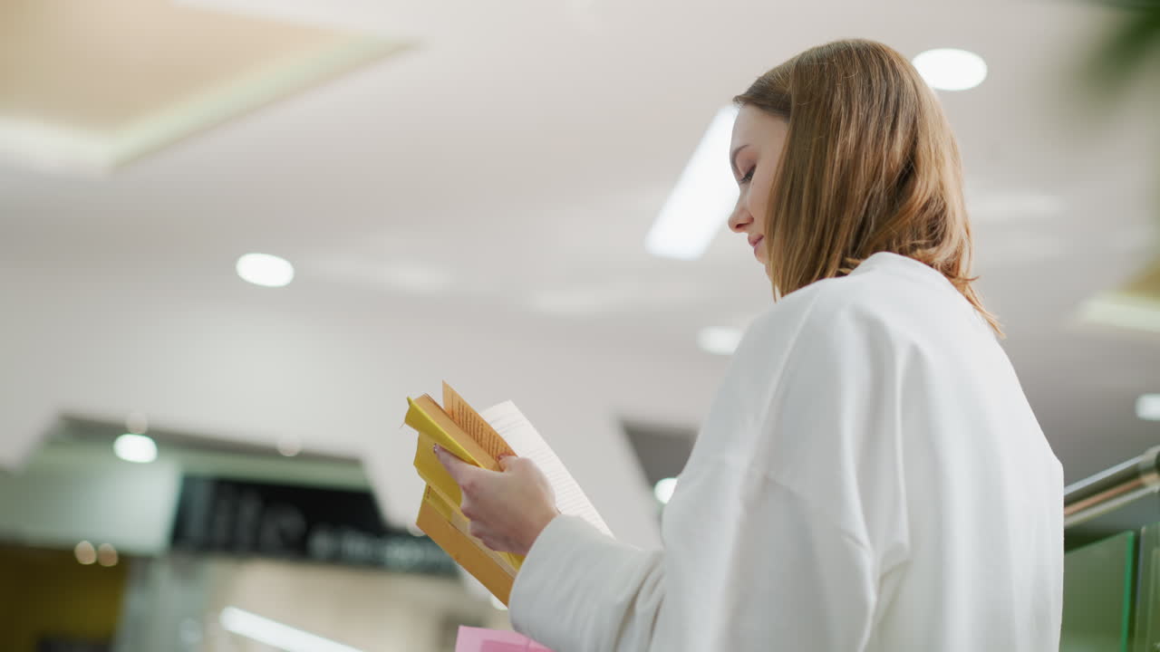 primer plano de una mujer joven leyendo un libro cubierto de amarillo en el interior, profundamente enfocado, con luz suave iluminando su perfil y el techo moderno