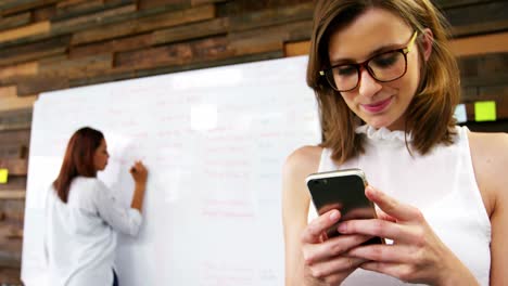 business executive using mobile phone while colleague writing on white board