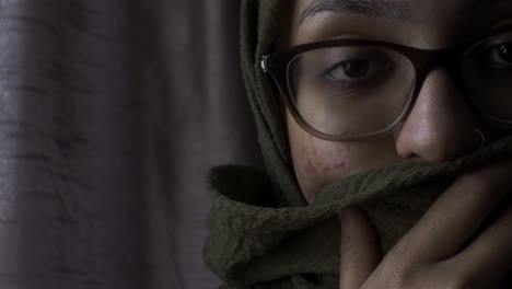 mujer con gafas sosteniendo hiyab cubriendo su boca mirando a la cámara