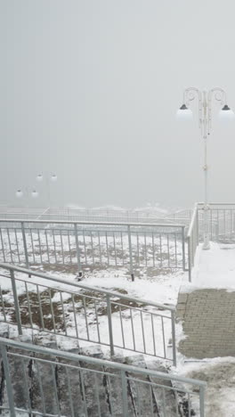 foggy urban winter setting with light poles and snow covered iron railings framing snowy staircase and raised platform, muted tones and soft diffuse lighting evoking tranquil scene
