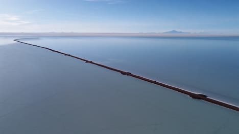 Aerial view: Road extends into shallow Uyuni Salt Flat lake, Bolivia