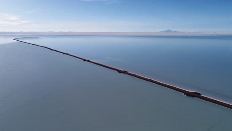 aerial view: road extends into shallow uyuni salt flat lake, bolivia