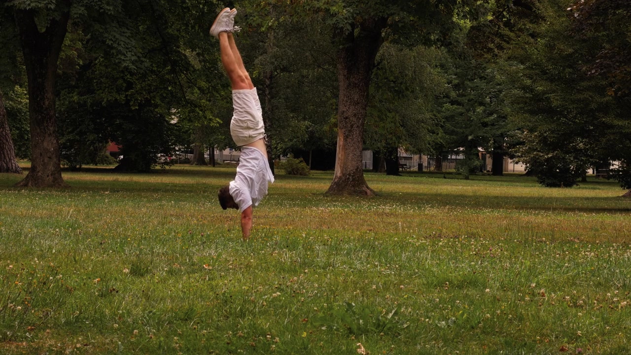 Young man performs a handstand on the grass while having fun in a green park. Active summer moment showing balance, fitness and outdoor recreation.