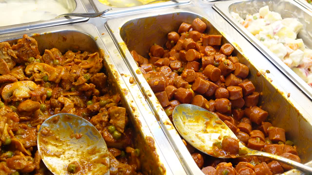 salchichas y otros platos de comida en una línea de buffet