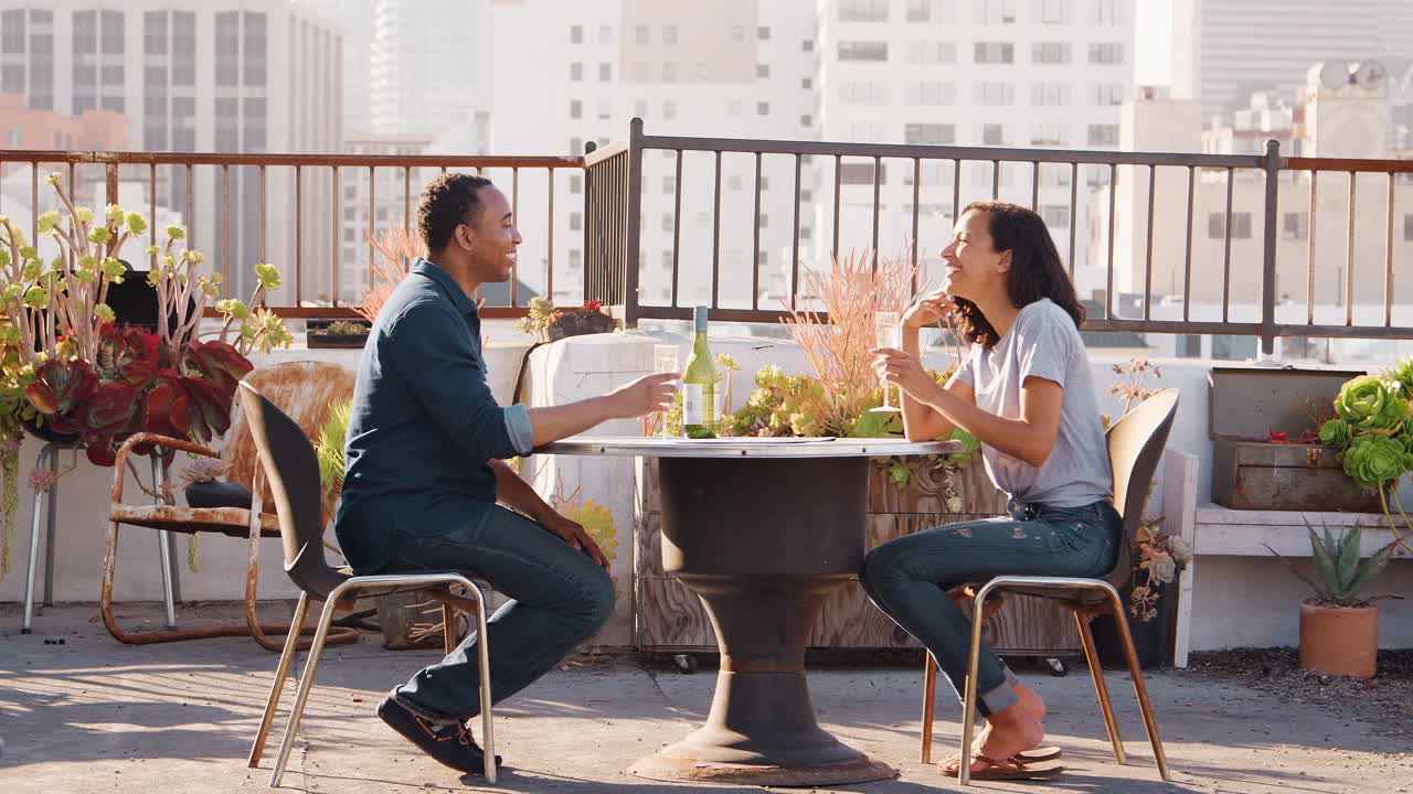 pareja bebiendo vino y haciendo brindis en la terraza de la azotea con el horizonte de la ciudad en el fondo