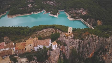 aerial drone cinematic 4k footage of a battlement and a village on top of a rock where a large reservoir of turquoise water can be seen