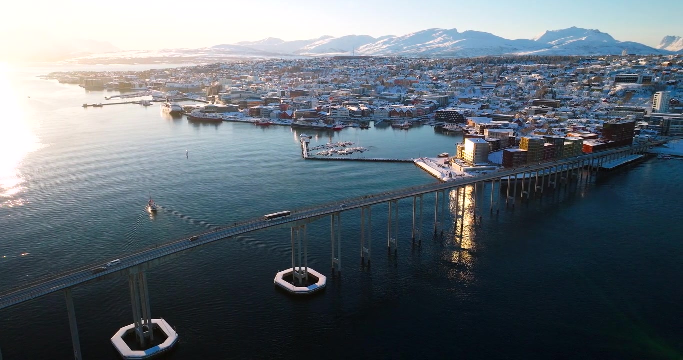 Norveç, Tromso'da kış güneş ışığında, Tromso köprüsü yakınında ve karla kaplı şehrin yanında yelken açan Hermes II teknesi. Havadan drone panoramik görünümü.