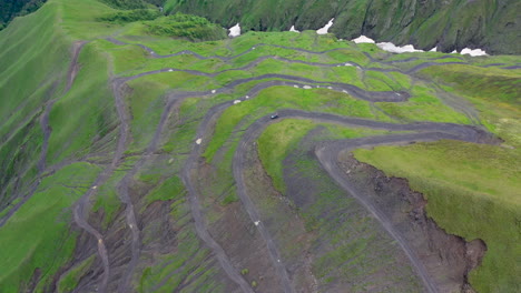 Cinematic-rotating-drone-shot-of-vehicle-driving-on-the-Road-to-Tusheti,-one-of-the-worlds-most-dangerous-roads