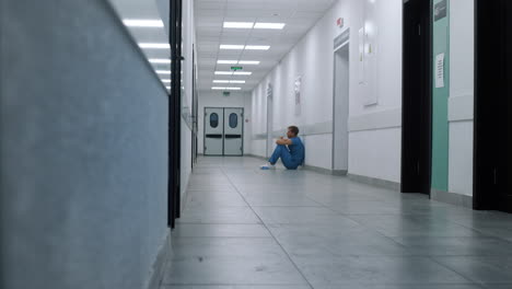 professional medic resting alone in hospital corridor. surgeon sitting on floor.