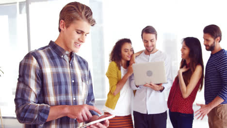 Executive-using-digital-tablet-while-colleague-discussing-in-background