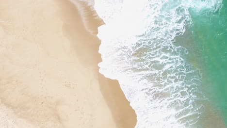 aerial view waves break on white sand beach