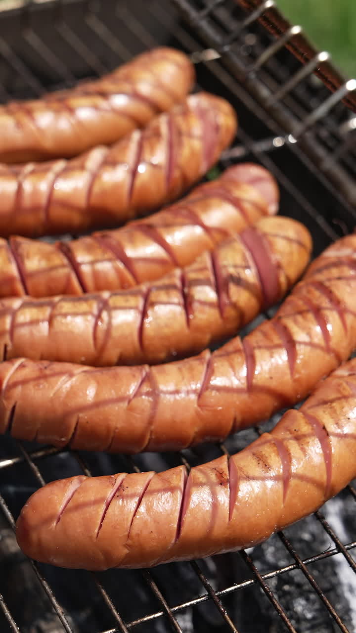 Roast wiener on a barbecue grill on charcoal. Cook turns over hot grilled sausages with a food tong in the garden in summer. Delicious food for a picnic. Vertical video