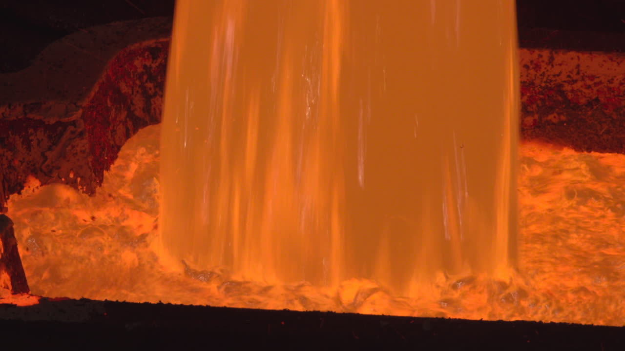 Metallo fuso arancione brillante che cola in fonderia industriale.