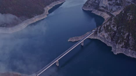 Enthüllen-Sie-Eine-Aufnahme-Einer-Brücke-Im-Piva-Lake-Canyon-In-Montenegro-Mit-Niedrigen-Wolken,-Aus-Der-Luft