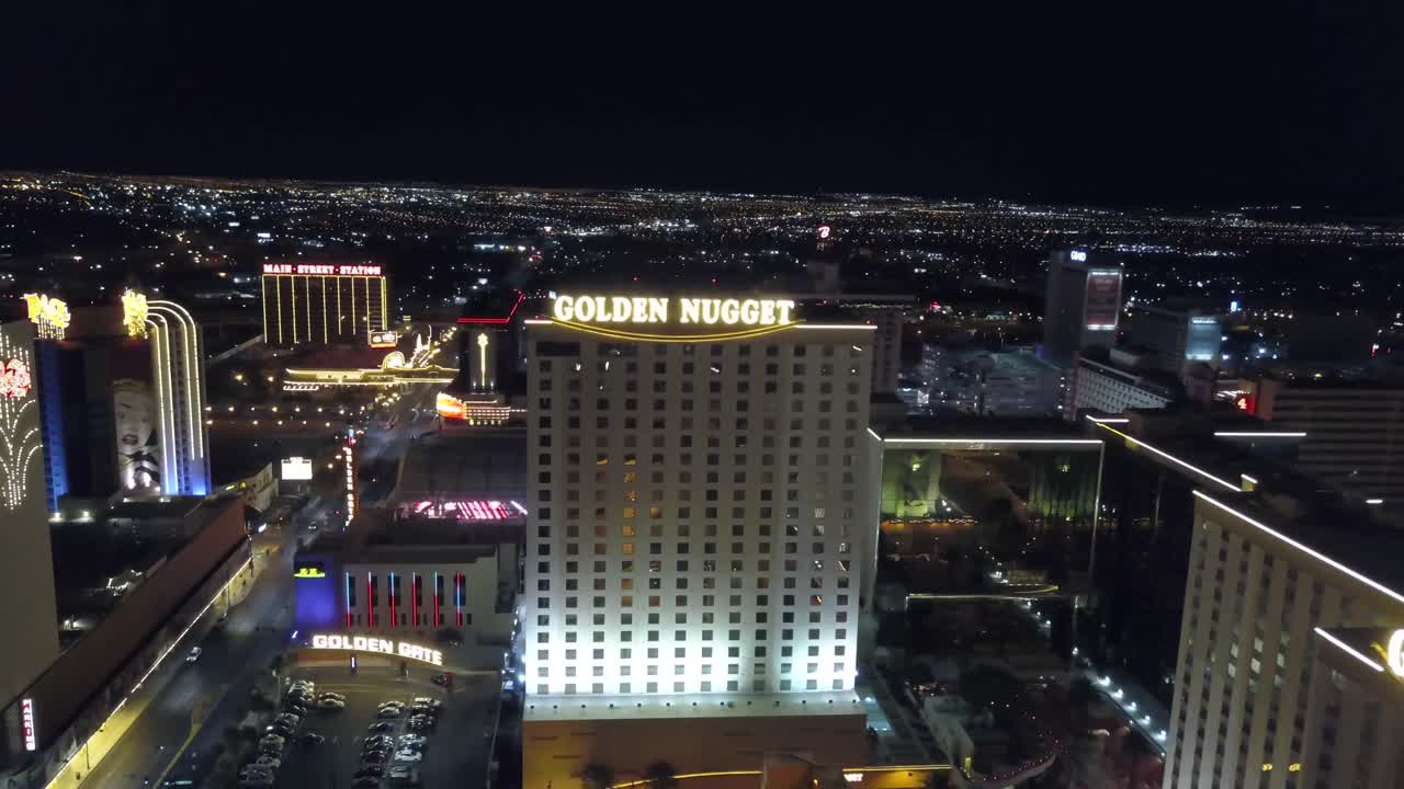 4K AERIAL: Aerial shot heading away and upwards from the Golden Nugget Hotel and Casino in Las Vegas with the city lights in background at dusk