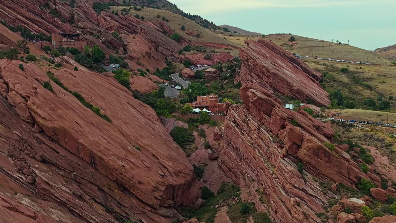 Drone descends over red sandstone cliffs surrounding Red Rocks Amphitheatre Colorado revealing desert horizon and terrain