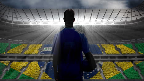 animation of rear view of football player holding ball over brazilian flag in sports stadium