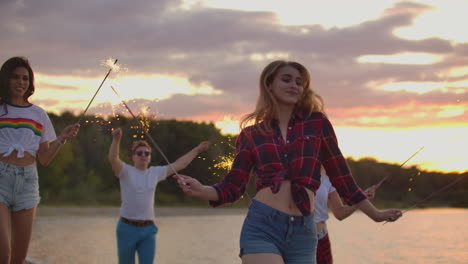 la chica está bailando con grandes luces bengalíes en sus manos en la playa de arena con sus amigos. esta es una hermosa noche de verano en la fiesta al aire libre.