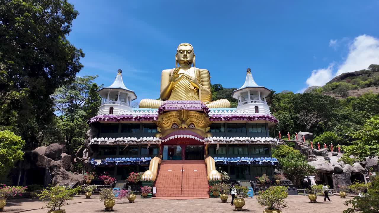 Dambulla Golden Temple with its giant gold Buddha statue in Sri Lanka, captured during a clear, sunny day. Tilt Up Shot